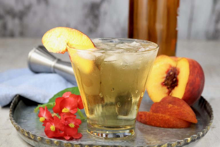 Peach Old Fashioned cocktail on a tray with begonia flowers