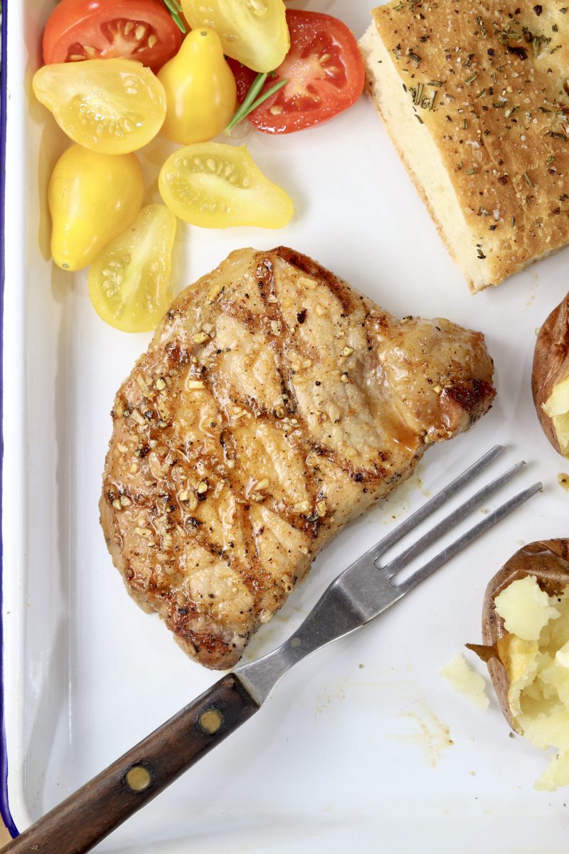 Honey BBQ Pork Chops on a white plate with a fork, sliced tomatoes, focaccia bread