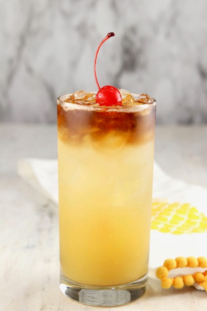 Collins glass with pineapple rum punch, garnished with a maraschino cherry