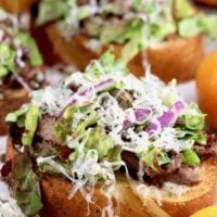 Open faced steak sandwich topped with lettuce, red onion, parmesan and steak sauce
