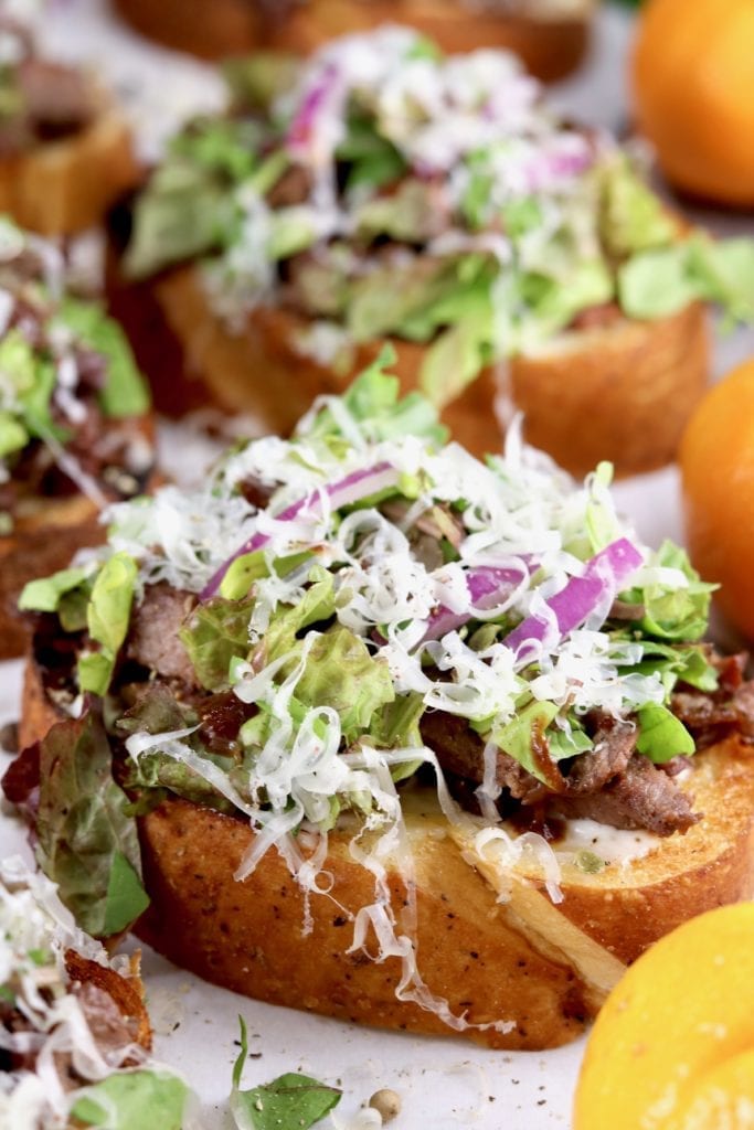 Open faced steak sandwich topped with lettuce, red onion, parmesan and steak sauce