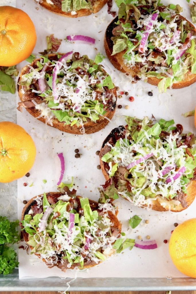 Overhead shot of tray of open faced steak sandwiches with lettuce and cheese