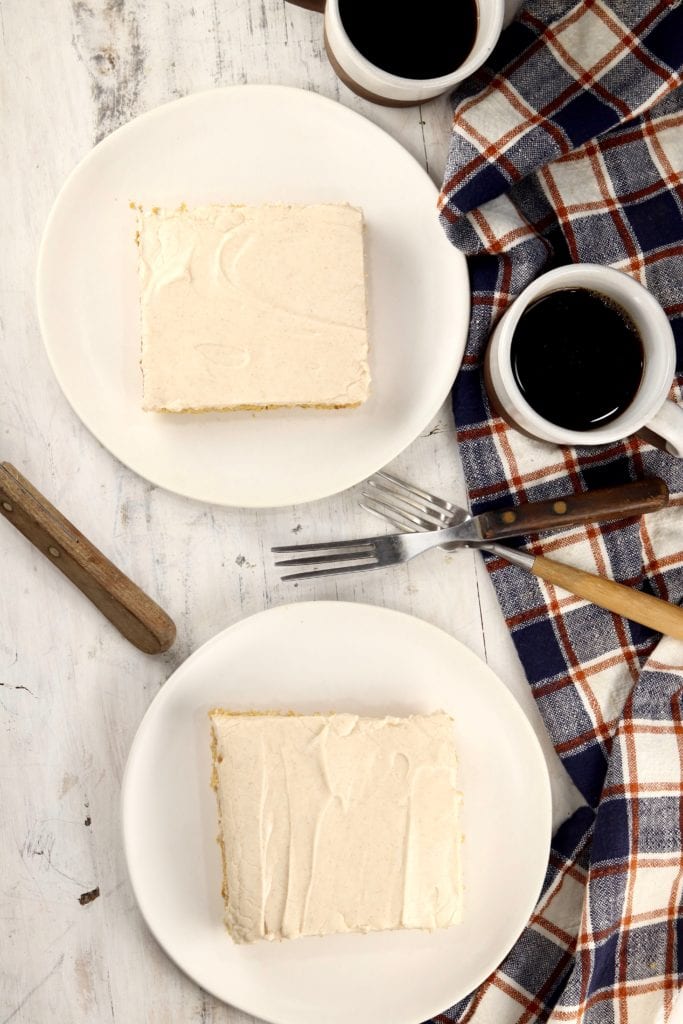 two slices of sheet cake on saucers with 2 cups of coffee