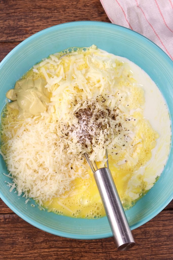 Filling for quiche in a blue bowl with a whisk