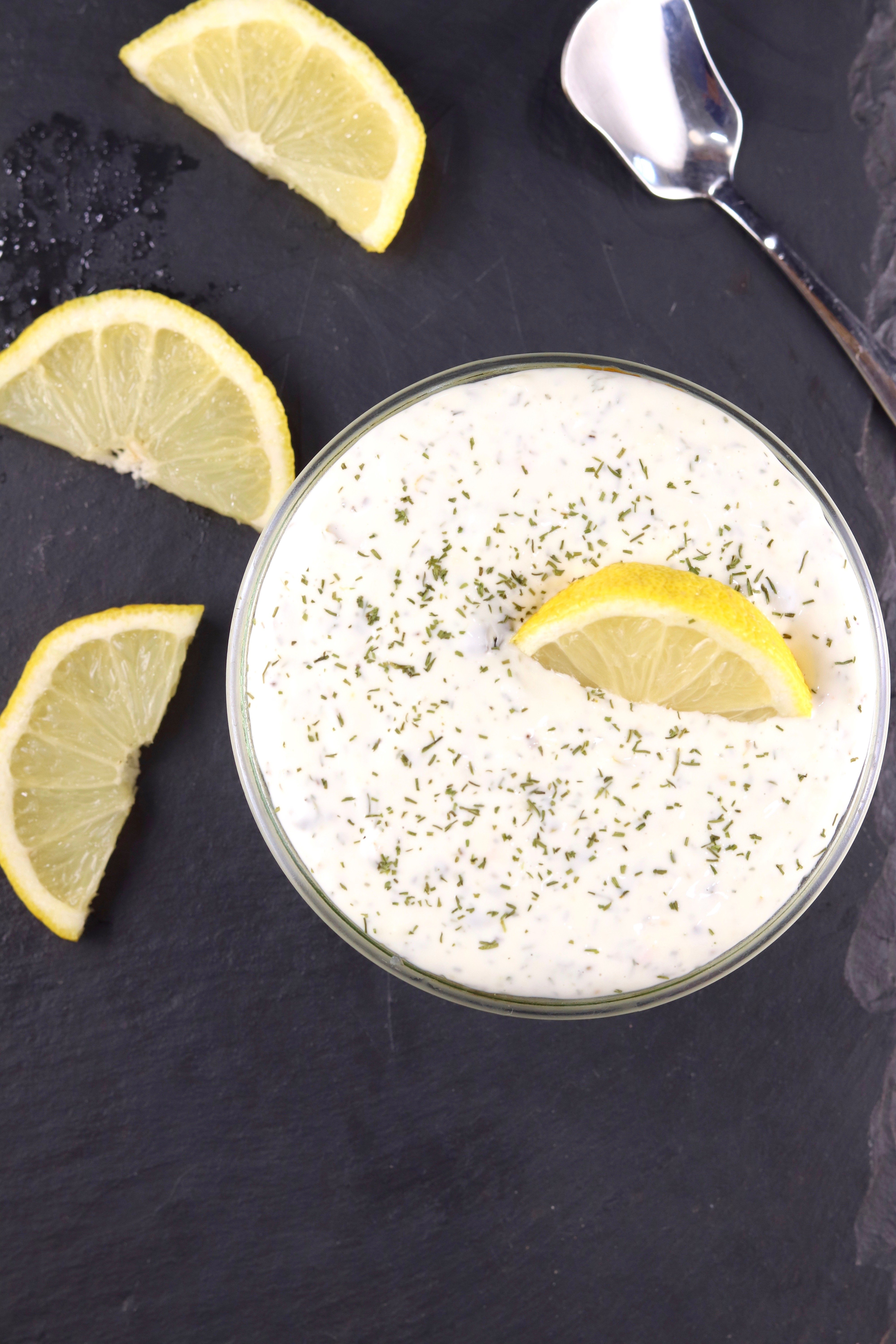 homemade tartar sauce with dill and lemon slices on a slate board.