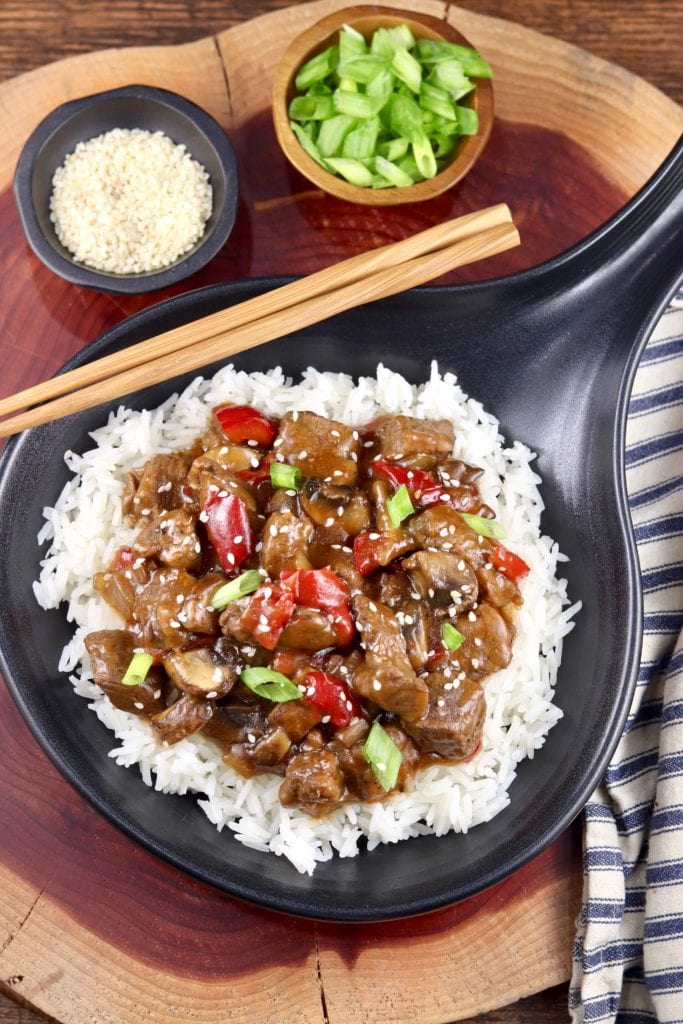 Black skillet with Teriyaki Steak over rice, bowl of green onions and bowl of sesame seeds