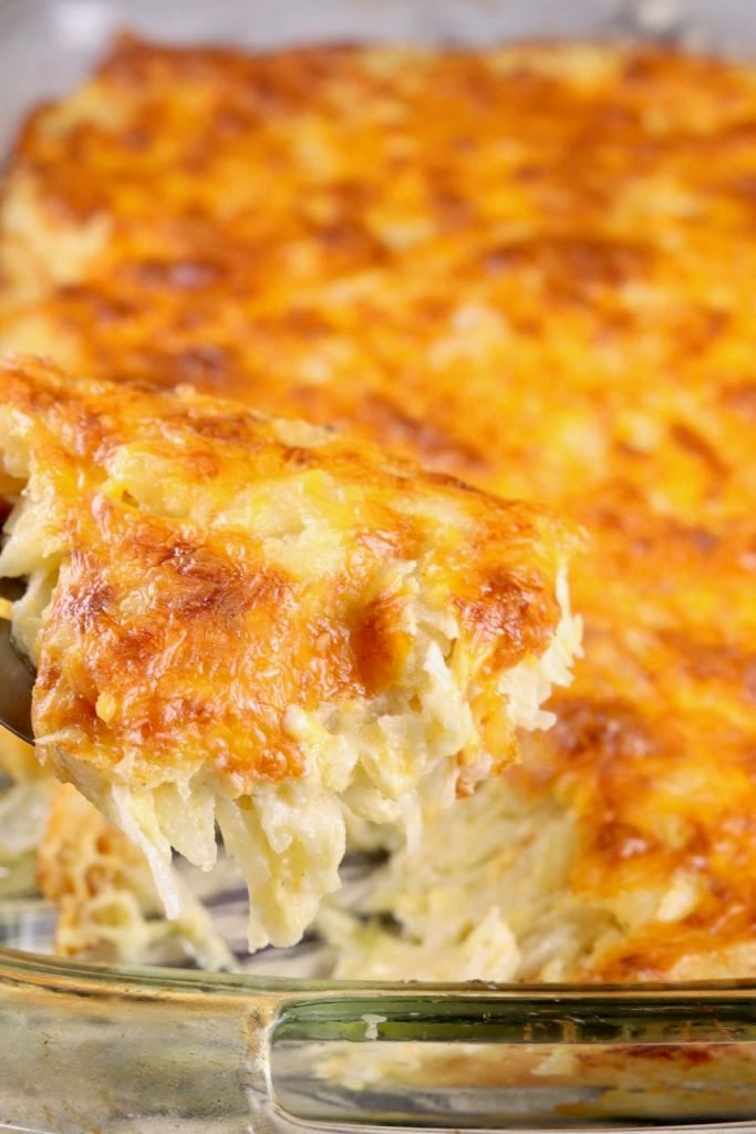 Cheesy Hashbrown Casseole in a clear baking dish, scooped with a spatula