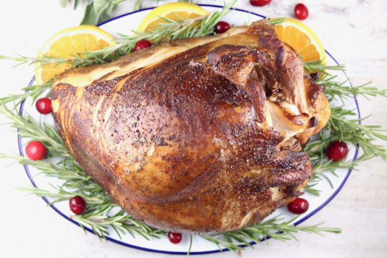 Smoked Turkey Breast on a platter with orange slices, fresh rosemary and cranberries