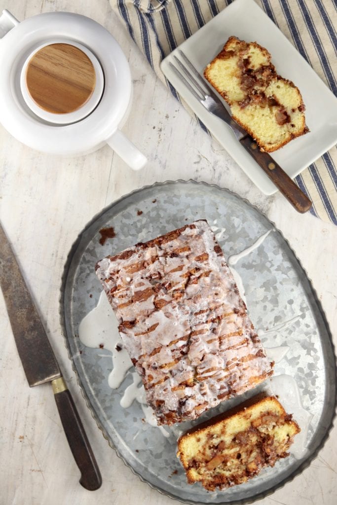 Overview of loaf of apple fritter cake on platter and slice of cake on a plate