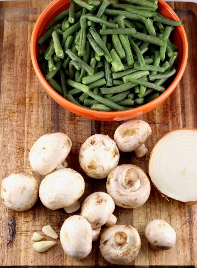 Fresh green beans in an orange bowl, whole button mushrooms and half of an onion