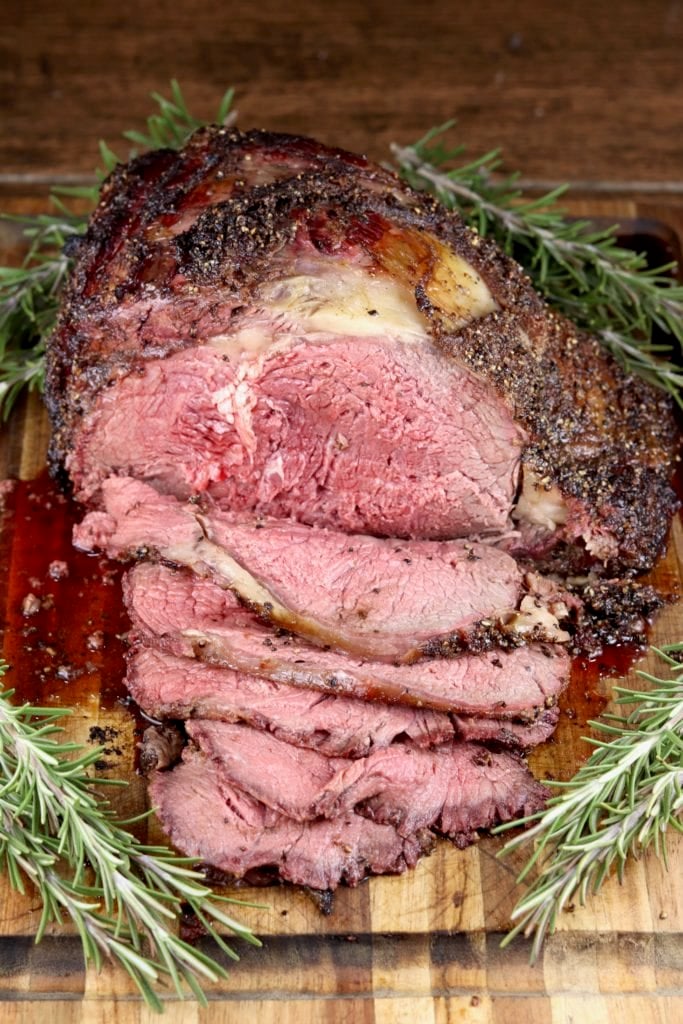 Prime Rib Roast sliced on a cutting board with fresh rosemary garnish