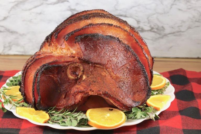 Maple Glazed Ham on a platter with fresh herbs and orange slices