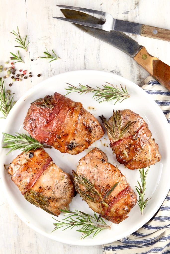 Plate of 4 grilled bacon wrapped pork chops with rosemary