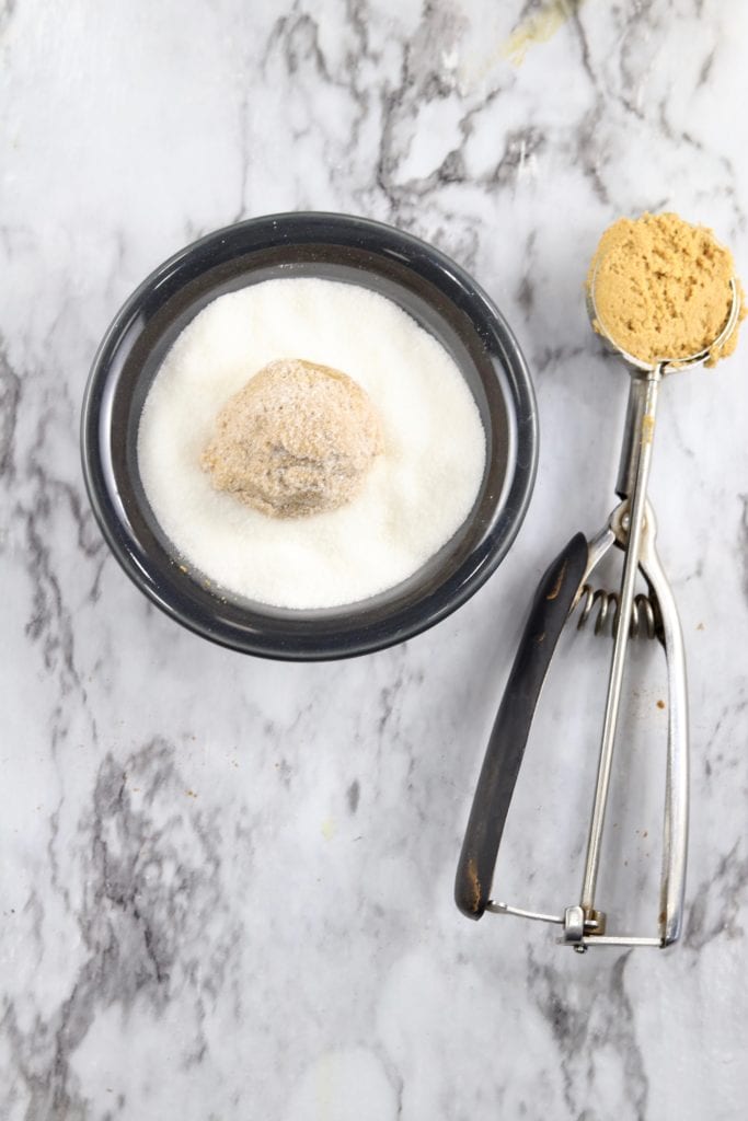 Cookie scoop and bowl of sugar with a scoop of molasses cookie dough