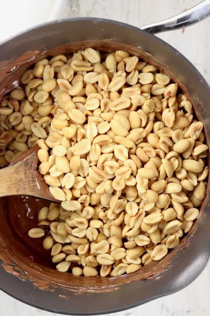peanuts poured into melted chocolate in a pan for clusters candy