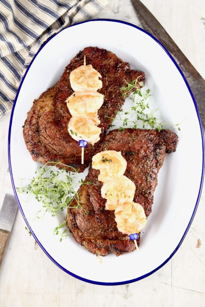 Garlic butter shrimp with ribeye steaks on a white platter
