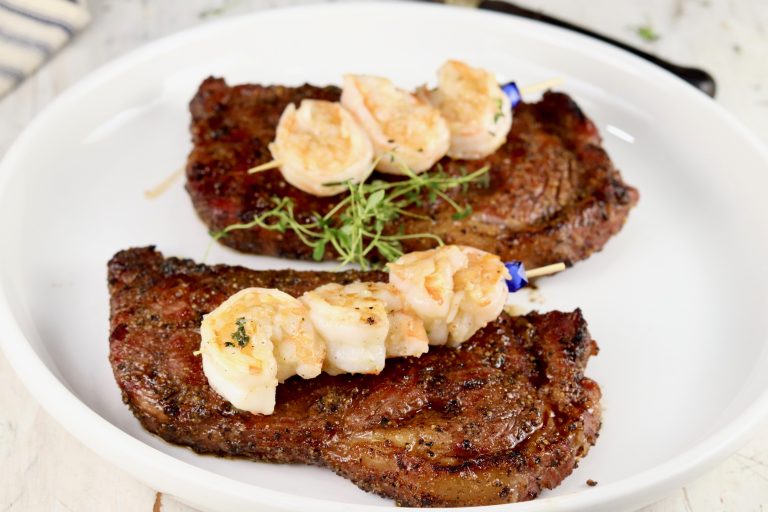 steak and shrimp on a white plateSurf and Turf is the ultimate dinner for entertaining guests or date night. Grilled ribeye steaks topped with garlic butter shrimp is a hearty and delicious meal that is sure to impress.