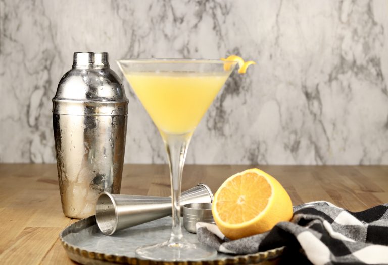 Bees Knees Cocktail in a martini glass with cocktail shaker and a lemon half