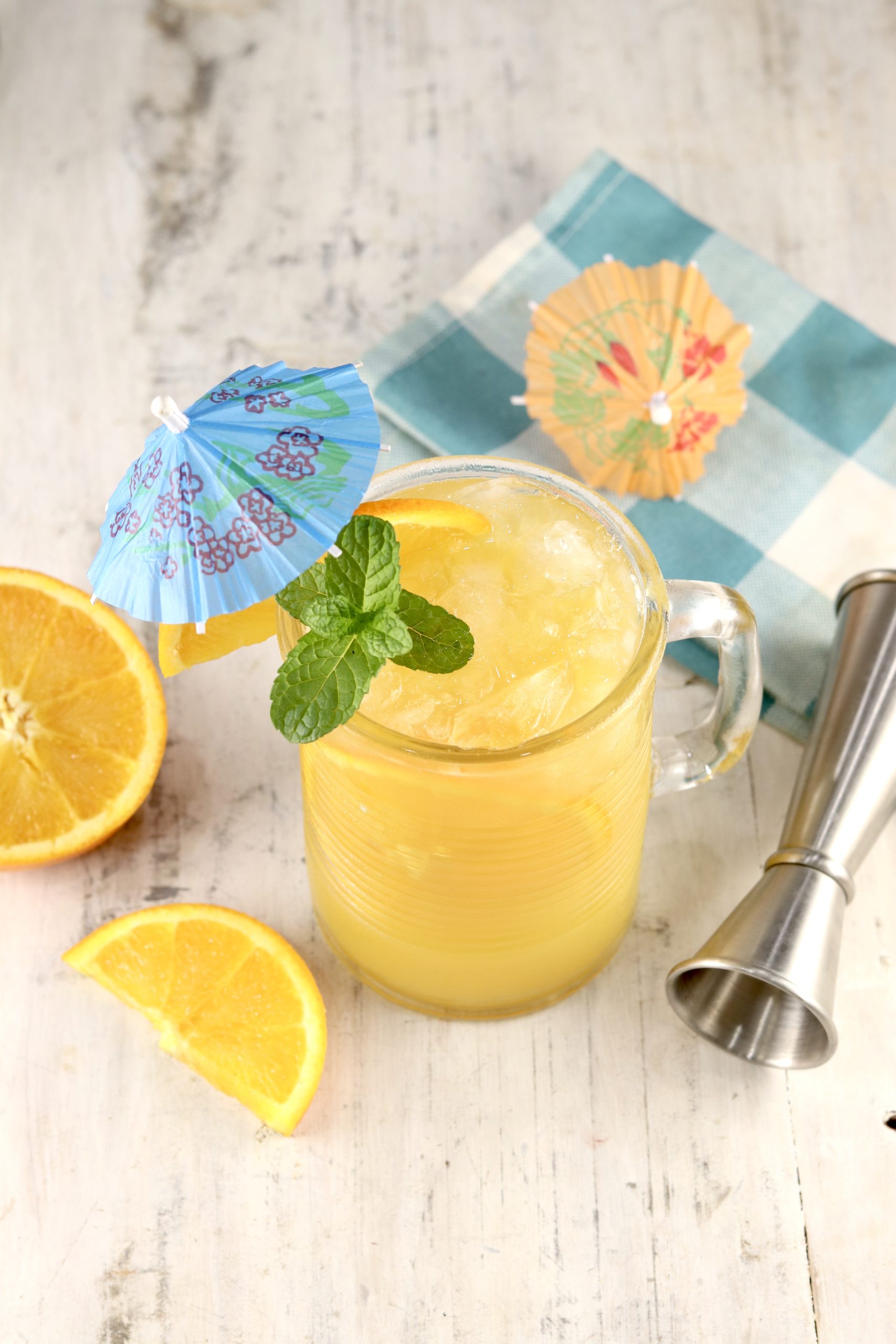 Brass Monkey Orange Juice cocktail overhead view sliced orange, mint and drink umbrella garnishes. Cocktail jigger and blue napkin