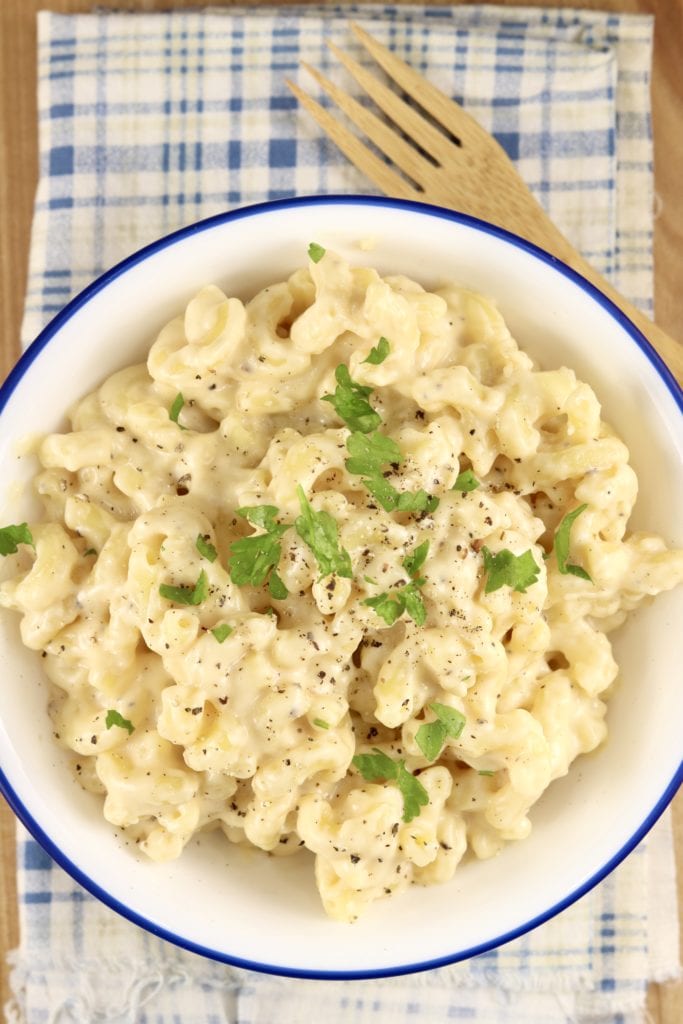 Bowl of macaroni and cheese garnished with parsley, bamboo fork
