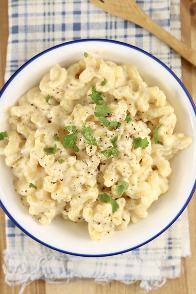 Macaroni and Cheese in a blue rimmed white bowl. On a plaid napkin, bamboo fork on the side
