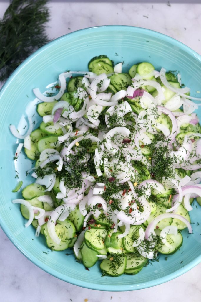 Sliced cucumbers, red onion, fresh dill and red pepper flakes in a blue bowl
