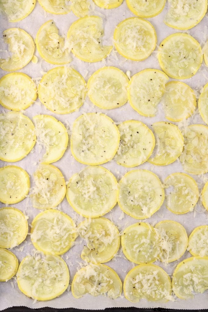 Sliced squash sprinkled with Parmesan cheese on a lined baking sheet
