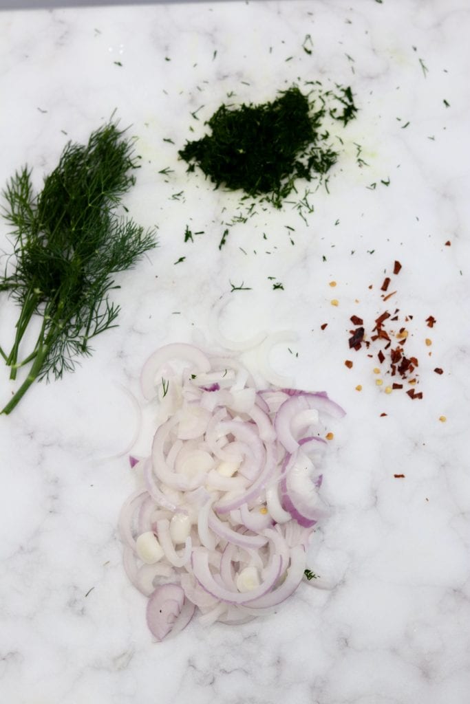 Chopped fresh dill, red onion and red pepper flakes on a marble board
