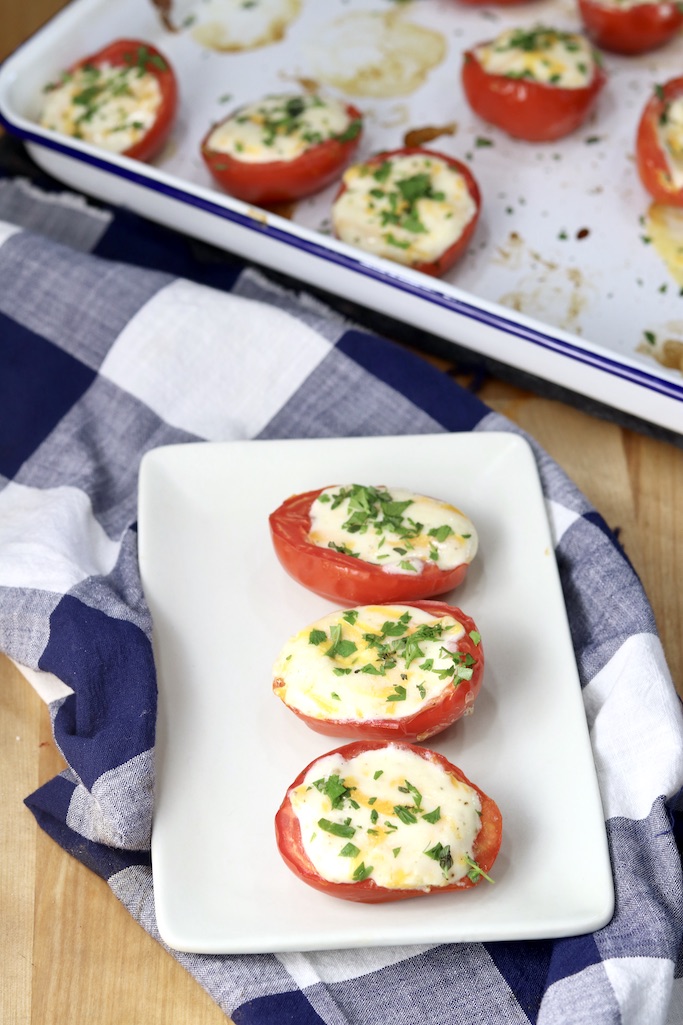 3 cheese stuffed Roma tomatoes on a small plate - baking pan of tomatoes in background