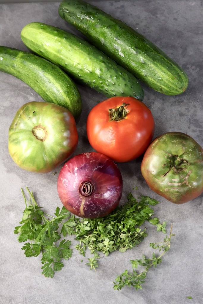 Cucumbers, tomatoes, red onion and fresh herbs on a gray board