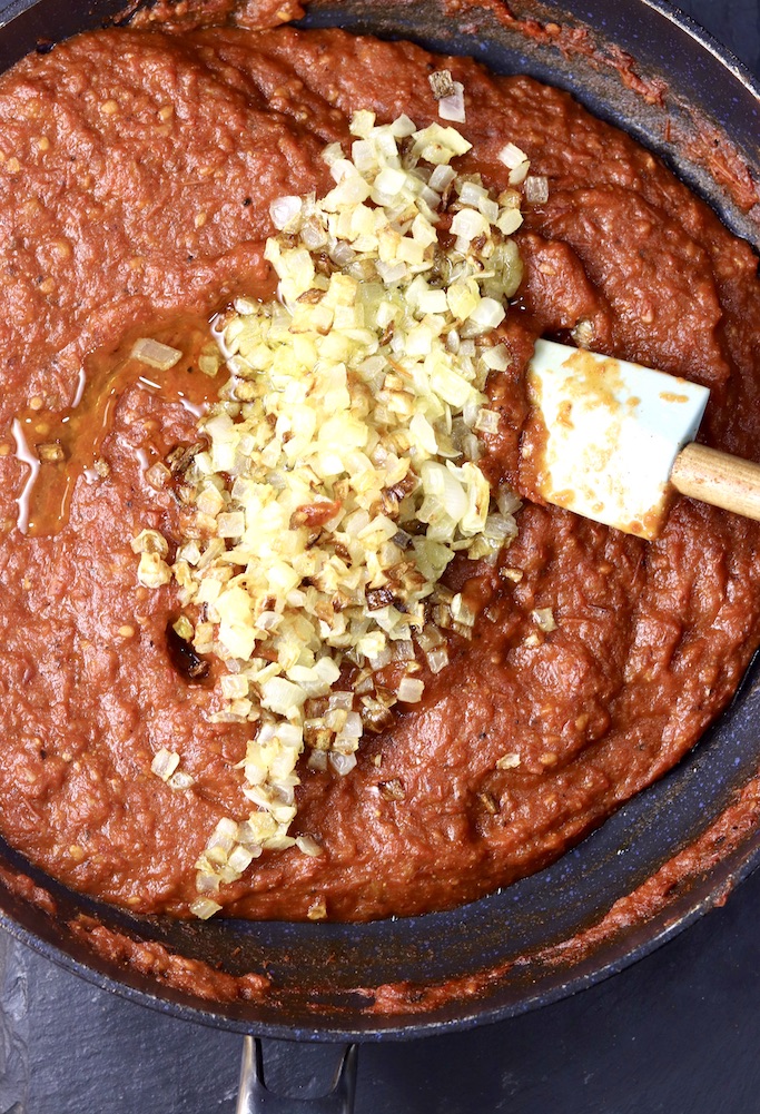 Pan of tomato sauce with cooked onions and a spatula