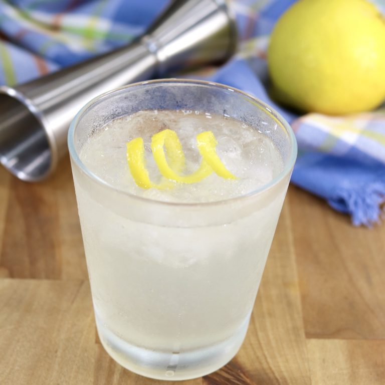 Gin Sour Cocktail garnished with a lemon twist, jigger and whole lemon in the background
