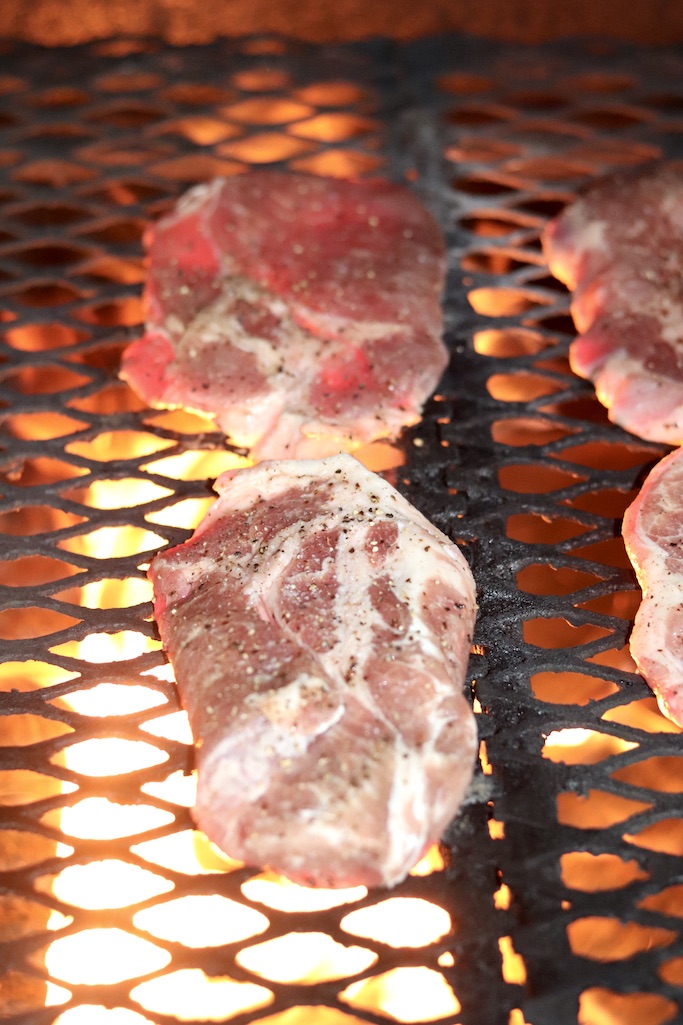 grilling pork steaks over wood fired grill- flames showing
