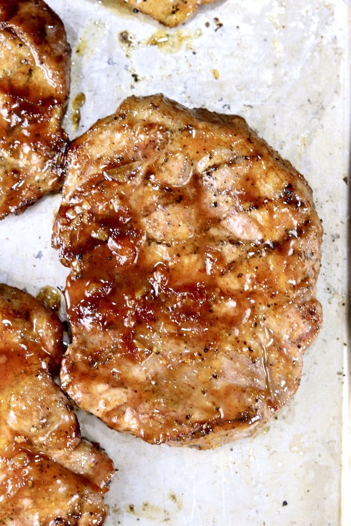 Peach BBQ glazed pork steaks on a baking sheet with grill marks, close up view