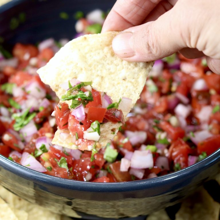 Pico de Gallo in a black bowl, dipped with a tortilla chip