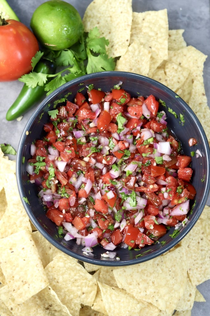 Pico de gallo in a black bowl, surrounded by tortilla chips, tomato, jalapeno and cilantro