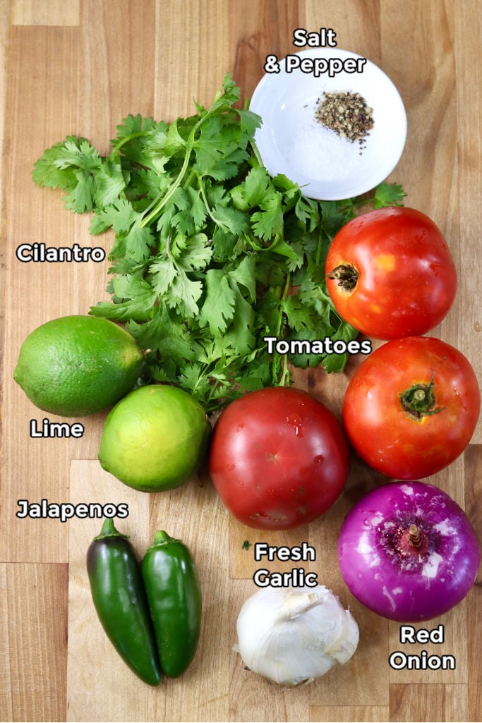 Ingredients for Pico de Gallo - limes, cilantro, tomatoes, red onion, garlic, jalapenos, salt and pepper in a pinch bowl