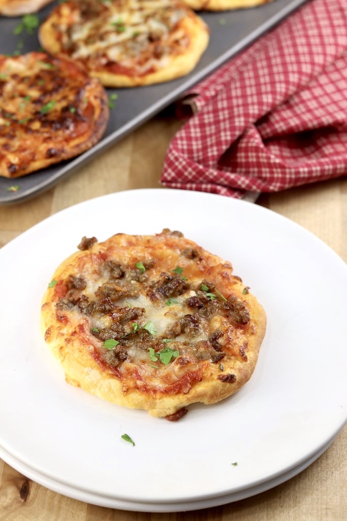 Air Fryer Mini pizza on a white plate - tray of pizzas in background with red napkin
