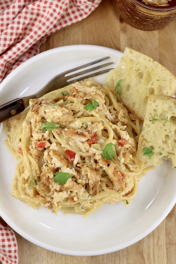 Cheesy Chicken Spaghetti on a white plate, fork and garlic bread, red napkin in corner