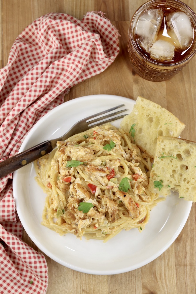 Overhead view of plate with chicken spaghetti and garlic bread. Glass of tea and red napkin.