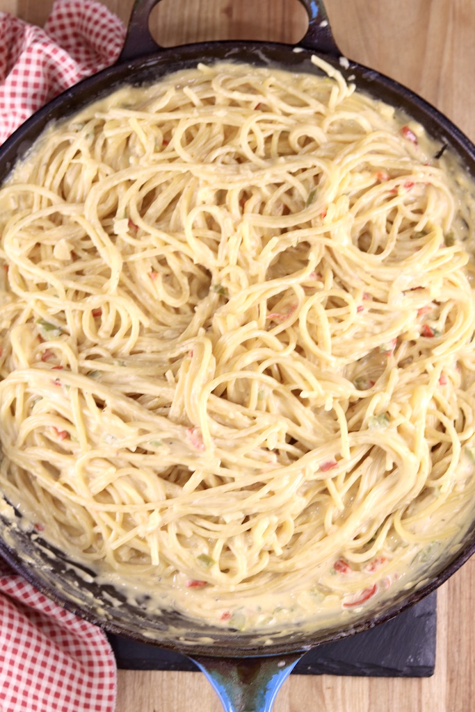 Spaghetti mixed into cheese sauce in a skillet