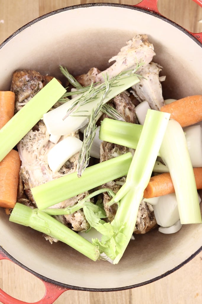 Homemade Chicken Broth made with chicken carcasses, celery, onions and carrots Dutch oven with chicken carcass, celery, carrots, onions and garlic