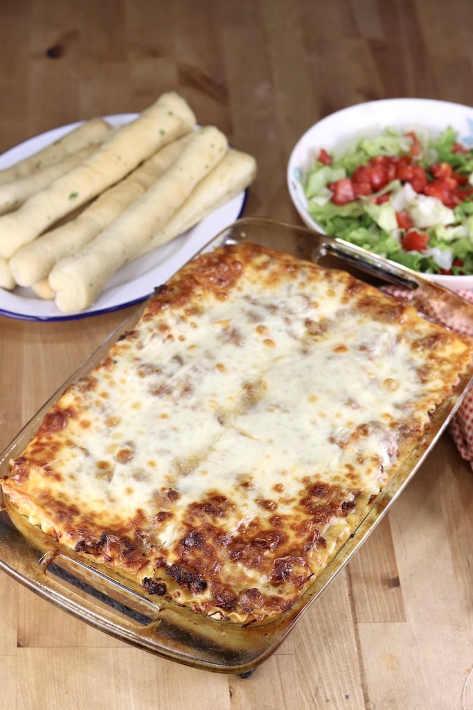 9 x 13 casserole with baked lasagna, plate of breadsticks, salad with tomatoes
