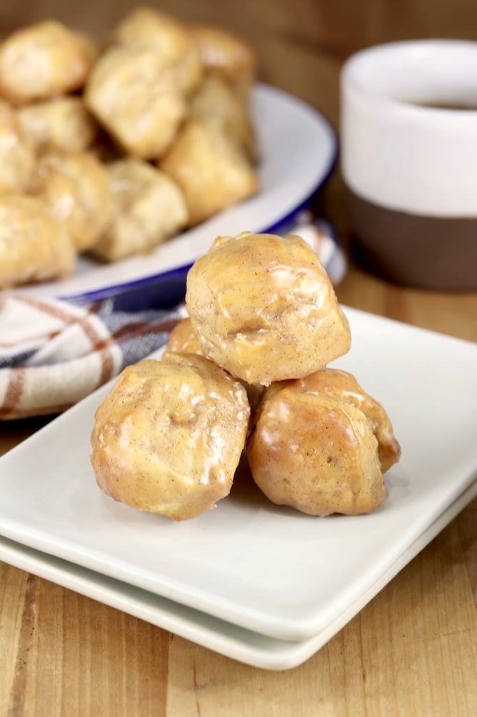 Plate of 3 donut holes with maple glaze, platter of donuts in background with coffee