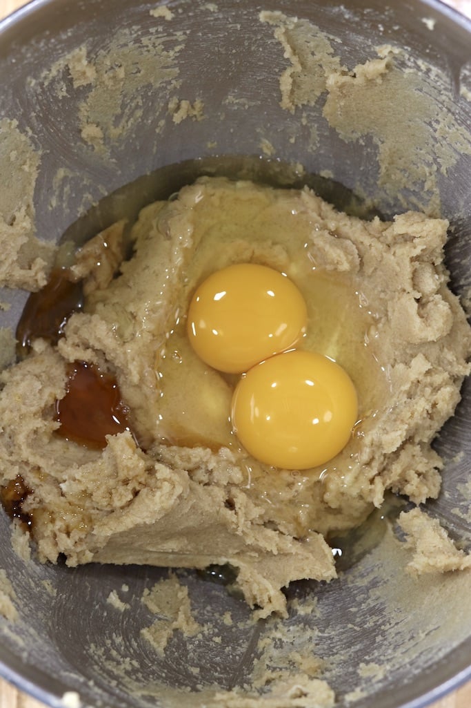 Adding 2 eggs and vanilla to cookie batter in a bowl