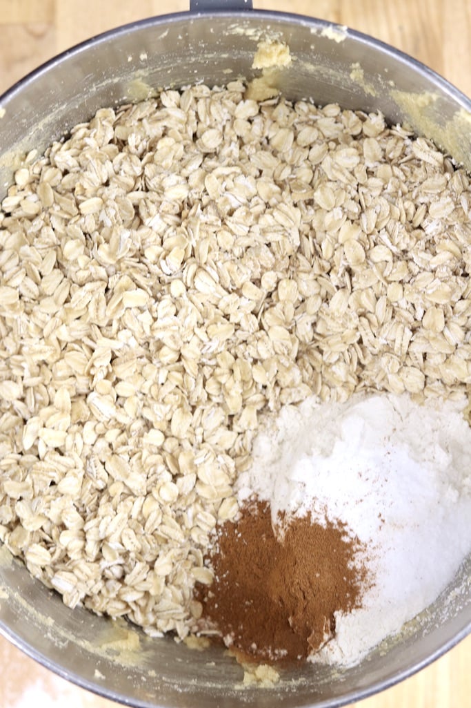 Adding old fashioned oats, baking soda and cinnamon to cookie batter in a bowl