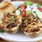 Pulled pork twice baked potatoes with salad and bread on a white plate, close up view