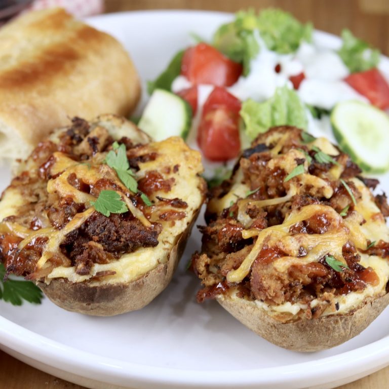 Pulled pork twice baked potatoes with salad and bread on a white plate, close up view