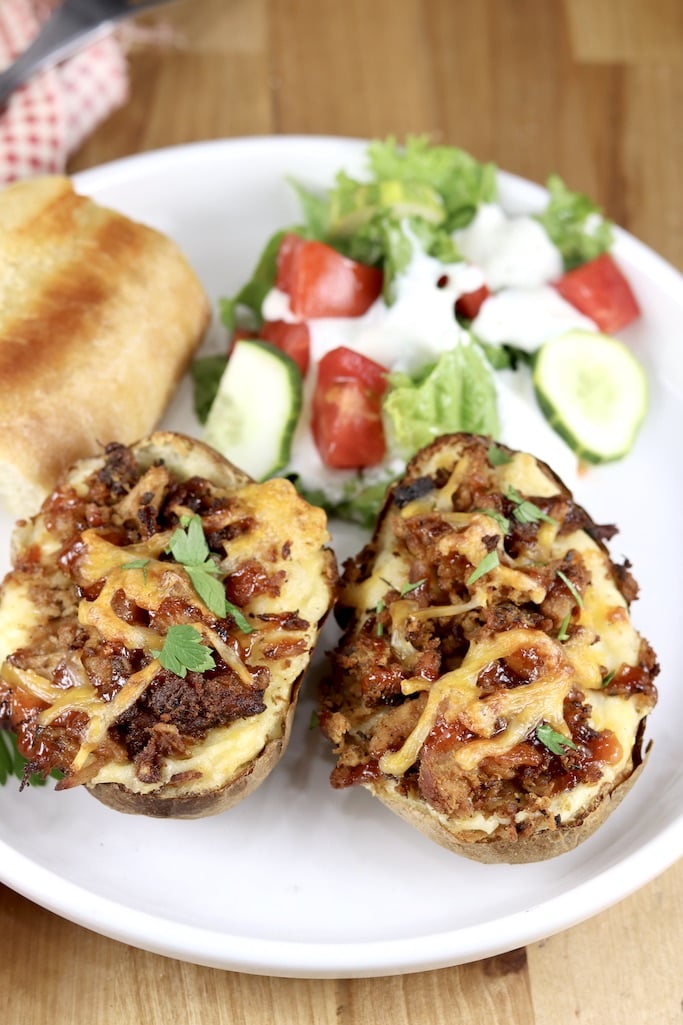 Smoked Pork topped twice baked potatoes on a white plate with salad and bread