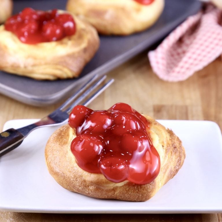 Cherry Cheese Danish on a white plate with a fork more pastries in background